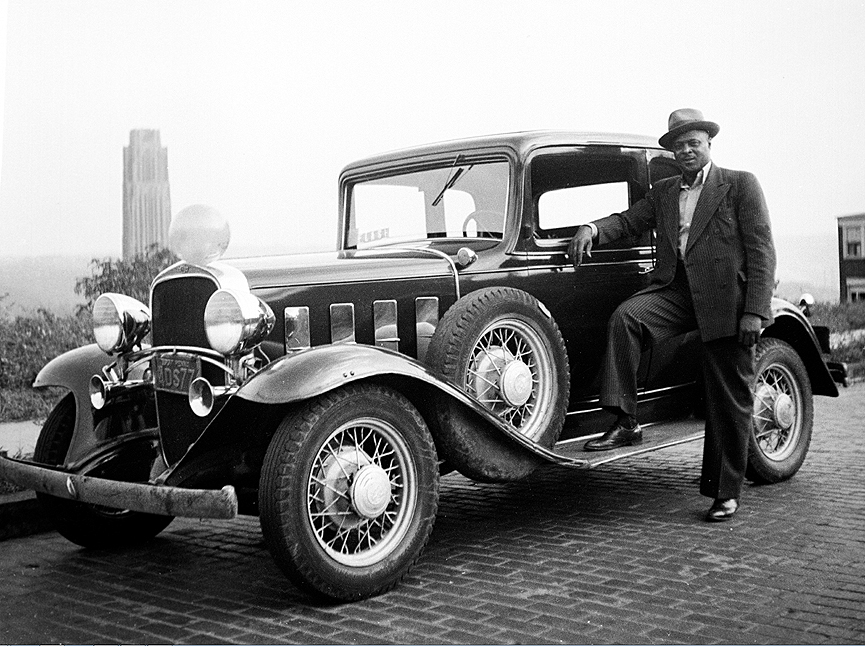 Un hombre posando frente a su coche con la Cathedral of Learning de Pittsburgh al fondo, 1937. Charles Harris
