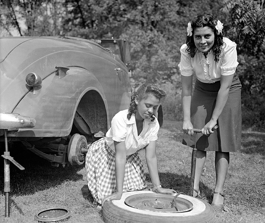 Dos jóvenes inflando la rueda de repuesto de su automovil tras un pinchazo, en 1947. Charles Harris