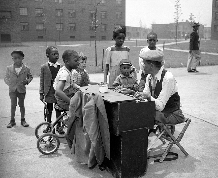 Un hombre tocando un pequeño piano en la calle enfrente de Terrace Village, en 1956. Charles Harris
